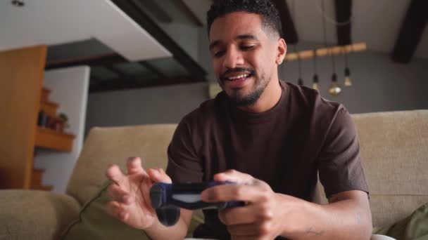 Van beneden vrolijke etnische Afro-Amerikaanse man glimlachen en videospel spelen met joystick terwijl chillen op comfortabel bed thuis tijdens het weekend - Video