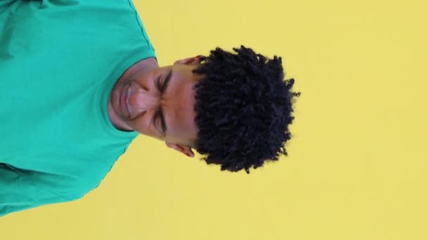 若いアフリカ系アメリカ人男性の肖像画 ドレッドロックと緑色のTシャツ 笑顔と黄色の背景からカメラを見ながら頭を上げる - 映像、動画