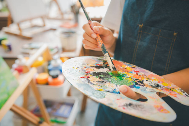 Close-up Art diák kezét egy ecsettel keverjük színek egy paletta a kezében, hogy akvarell festmény vásznon csinál néhány művészeti projektek - Fotó, kép