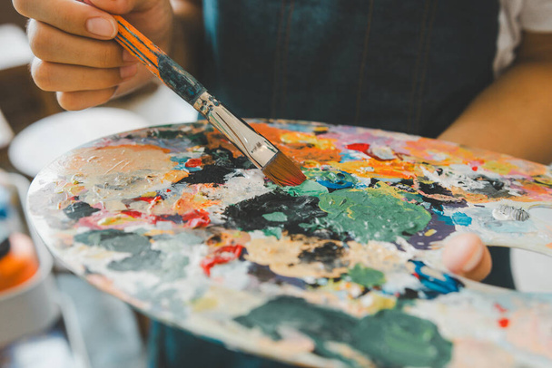 Close-up Mano de estudiante de arte usando un pincel para mezclar colores en una paleta en la mano para acuarela pintura sobre lienzo haciendo algunos proyectos de arte - Foto, Imagen
