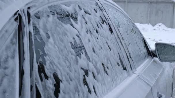 Washing luxury silver car on touchless car wash. Washing sedan car with foam self-service and high pressure water. Winter cleaning in car wash. Cleanliness and order in urban environment - Filmagem, Vídeo