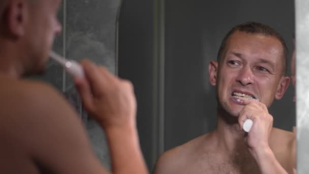 Egy fiatal férfi portréja, aki fehér fogat mos modern elektromos fogkefével, közelről. Fogászat, napi ellátás, szájhigiénia és fogtisztítás koncepciója. reggeli egészségügyi eljárások,, - Felvétel, videó
