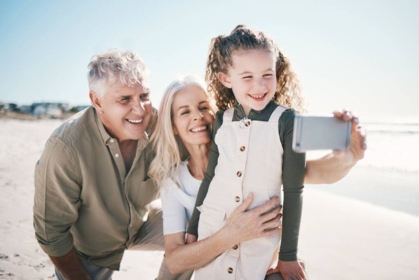 Family, selfie smile and beach holiday with grandparents and young girl together with travel. Happy, child and love at the sea and ocean with profile picture for social media on summer vacation. - Photo, Image