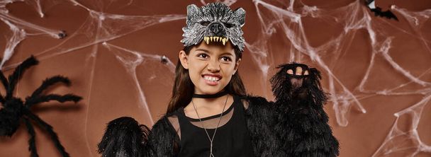 close up of preteen girl in black attire and wolf mask scaring with raised hands, Halloween concept - Photo, Image
