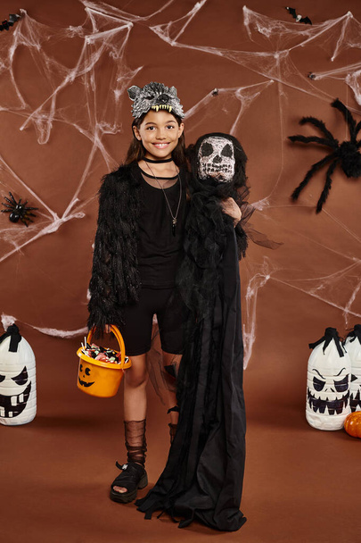 happy preteen girl in wolf mask with bucket of sweets and spooky toy, Halloween concept - Foto, Imagem