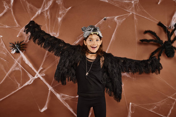 happy girl with opened arms in black faux fur attire with spiderweb on brown background, Halloween - Photo, Image