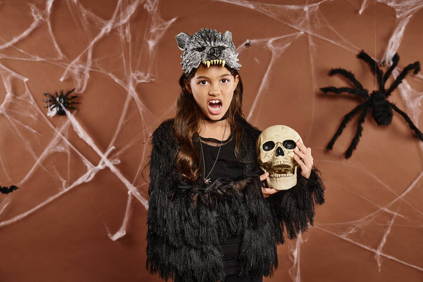close up menina surpreso com boca aberta segura crânio com fundo marrom, conceito de Halloween - Foto, Imagem