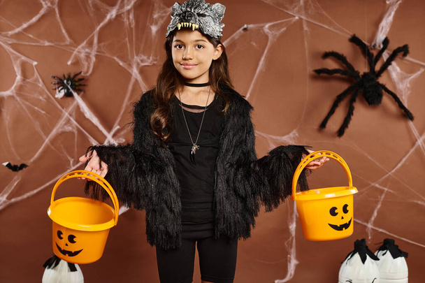 smiley kid in wolf mask with two pumpkin buckets on brown background with webs, Halloween, close up - Photo, Image