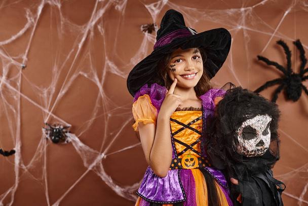 zbliżenie nastolatek dziewczyna w czarownica kapelusz z upiorny zabawka dotykając jej policzek i uśmiech, Halloween - Zdjęcie, obraz
