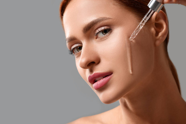 Beautiful young woman applying cosmetic serum onto her face on grey background, closeup. Space for text - Foto, imagen