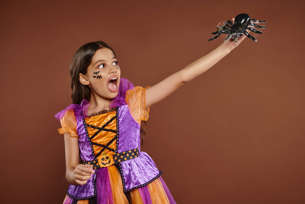 rémült lány Halloween jelmez nézi fekete pók és sikoltozik barna háttér, Október 31. - Fotó, kép