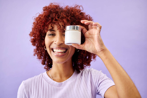 Portrait, beauty and cream for skincare with a woman holding a container in studio on a purple background. Face, smile and promotion of a product or serum for antiaging with a happy young model. - Photo, image
