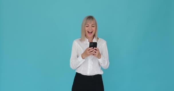 Kadın, sakin bir mavi arka planda telefonunu kullanırken kahkaha atarken yakalandı. Bulaşıcı gülüşü ve neşeli ifadesi, etkileşim sırasında eğlencesini ve mutluluğunu iletir.. - Video, Çekim