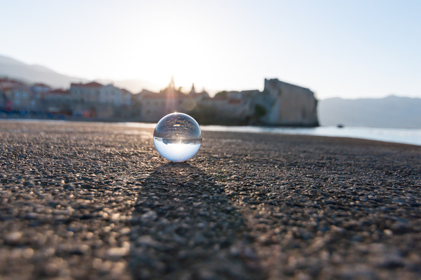 Стеклянный прозрачный шар на морском фоне и зернистой поверхности. Вода
 - Фото, изображение