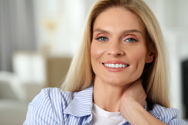 Портрет улыбающейся женщины средних лет с светлыми волосами в помещении - Фото, изображение