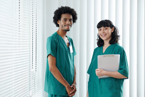 Tým zdravotních sester v zelených pláštích stojící na lékařské klinice a dívající se do kamery - Fotografie, Obrázek