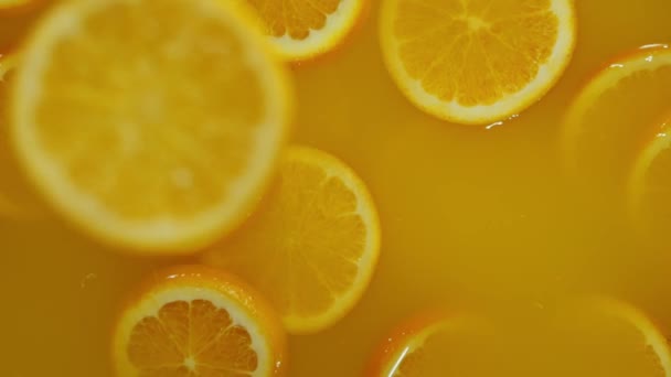 Lähikuva kuuluvat viipaloidut limetit, appelsiinit ja sitruunat veteen oranssilla pohjalla, tehdä cocktail sitrushedelmiä, juo kylmää limonadia, ammunta hiilihapotettua vettä viipaloidut hedelmät. - Materiaali, video
