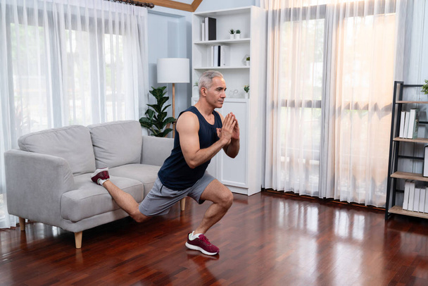 Aktif ve formda bir adam oturma odasında egzersiz yapmadan önce mobilya kullanarak ısınıyor ve esniyor. Emeklilikten sonra sağlıklı yaşam tarzı konsepti. Etki - Fotoğraf, Görsel