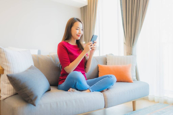 Porträt schöne junge Asiatin benutzt Smartphone auf Sofa im Wohnbereich im Schlafzimmer - Foto, Bild