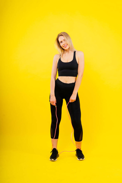 Fitness-Frau macht Sprungübungen mit Springseil auf buntem gelben Hintergrund. - Foto, Bild