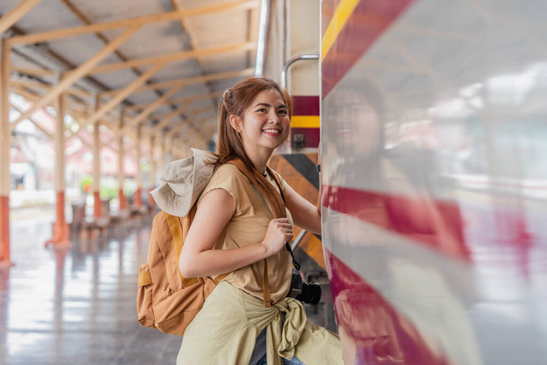 Piękny azjatycki podróżnik z plecakiem wsiadający do pociągu na peronie dworca kolejowego. - Zdjęcie, obraz