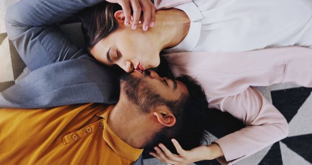 Omhels, boven en koppel kussen op de vloer uit liefde, zorg en comfort in relatie. Geluk, genegenheid en een man en vrouw die samen met een glimlach kussen voor geluk, huwelijk en romantiek. - Foto, afbeelding
