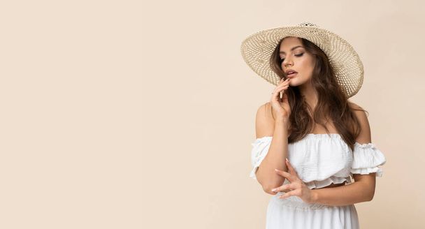 Очень красивая молодая женщина в соломенной шляпе и белом платье на сливочном фоне. - Фото, изображение