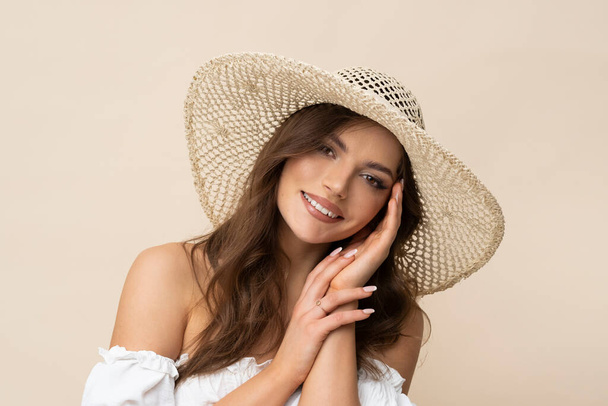 Zeer mooie jonge vrouw in stro hoed en witte boho jurk op romige achtergrond. - Foto, afbeelding