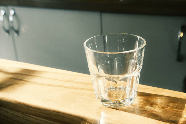 Un verre transparent à facettes sur une table dans un café, avec les rayons du soleil qui y brillent et réfléchissent - Photo, image