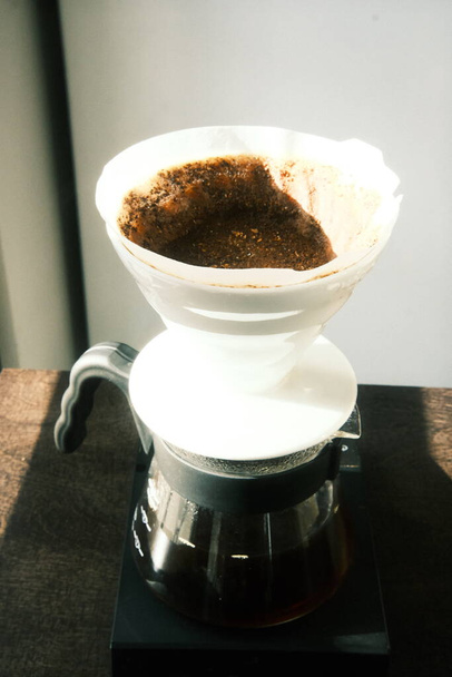 Zwarte koffie vers gegoten door een V-60 druppelaar in een glanzende glazen karaf - Foto, afbeelding