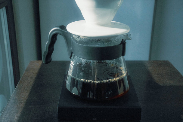 Темний кавовий еліксир тече з крапельниці V-60 у скляний декантер - Фото, зображення