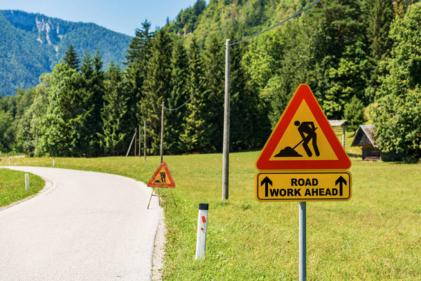 Carretera triangular anaranjada, roja y negra obra delante señal o obra en progreso señal, al lado de una carretera en mantenimiento (mal estado). - Foto, imagen