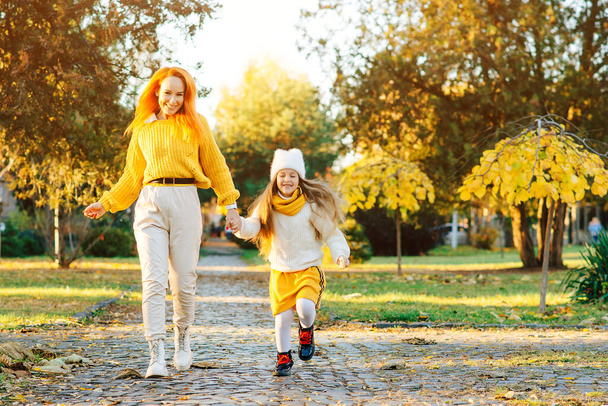 Kedves lány az anyjával, aki jól érzi magát a sétányon. Őszi szünidő, életstílus. Boldog család élvezi őszi időjárás a parkban. - Fotó, kép