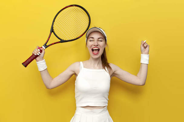 Tennisspielerin in Sportkleidung hält Tennisschläger in der Hand und jubelt über Sieg auf gelbem Hintergrund, Tennisspielerin in weißer Uniform feiert Erfolg und Glück und schreit - Foto, Bild