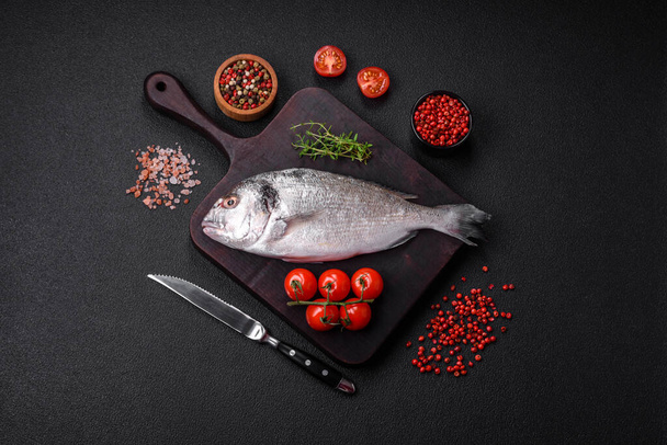 Νωπό ωμό ψάρι dorada με αλάτι, μπαχαρικά και βότανα σε σκούρο μπετόν φόντο - Φωτογραφία, εικόνα