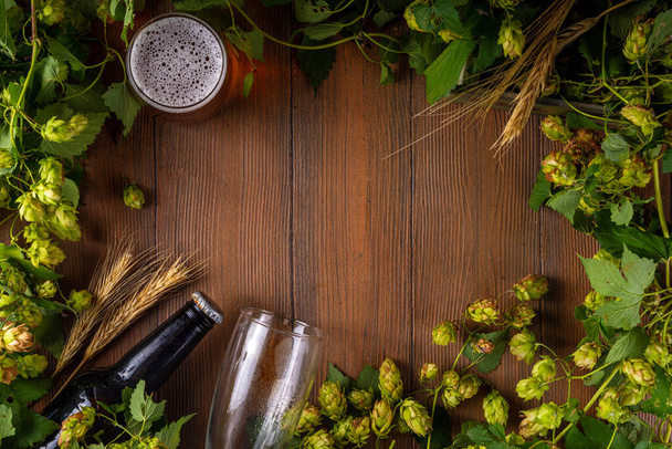 Bierfles en glas met hopbellen, vers ambachtelijk bier en ingrediënten, kopieerruimte op houten ondergrond - Foto, afbeelding