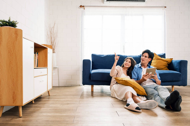 Atraktivní novomanželé sedí spolu na podlaze v obývacím pokoji a ukazují na kopírovací prostor v novém domově. Rodina spolu tráví čas poté, co se přestěhovala do nového domova. - Fotografie, Obrázek