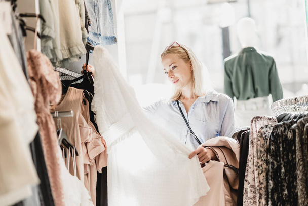 Nainen ostoksilla vaatteita. Nainen shopper tarkastellaan muodikas vaatteita sisätiloissa vaatekaupassa
. - Valokuva, kuva