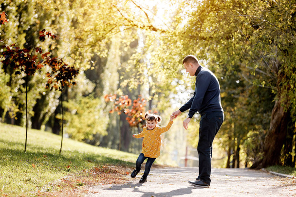 Dzień ojców. Szczęśliwy tata dobrze się bawi i kręci swoją córeczką na świeżym powietrzu w jesiennym parku. Samotny tatuś z dzieckiem relaksuje się i spędza razem czas. Dzień rodzinny i koncepcja dzieciństwa. Aktywne śmieszne gry - Zdjęcie, obraz