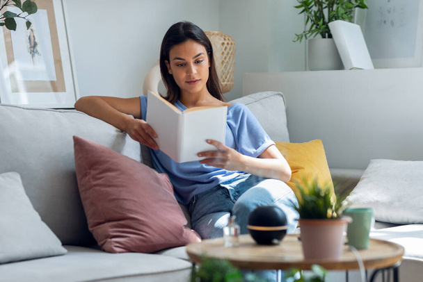 Shot of beautiful woman reading a book while essential oil aroma diffuser humidifier the air in living room at home - Foto, Imagem