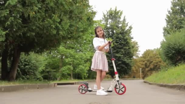 Маленька дівчинка вчиться їздити на електричному скутері. Їзда на скутері в міському парку. - Кадри, відео