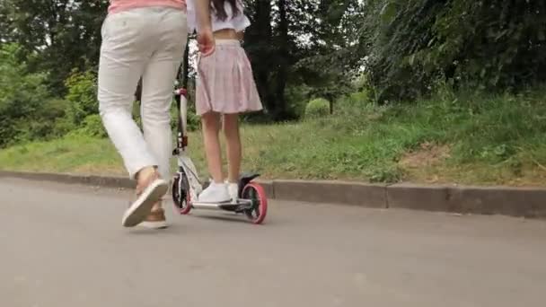Papá le enseña a su hija a montar un scooter eléctrico. Montar en una moto en un parque de la ciudad. Vida deportiva, niños alegres, padres cariñosos. - Metraje, vídeo