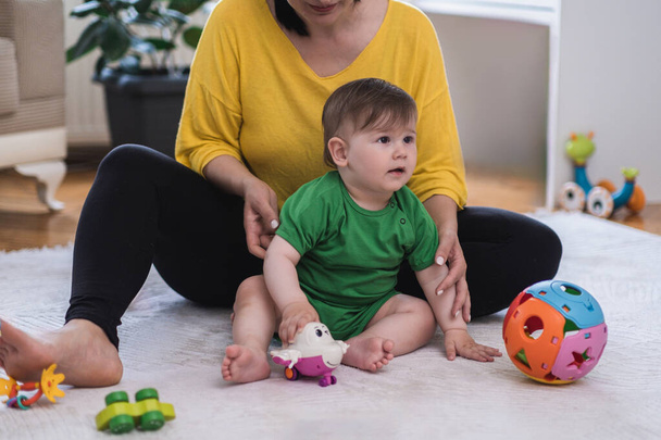 Gondoskodó anya és kedves kisfiú ül a puha fehér szőnyegen játszik az oktatási játékok nő élvezi időt a fiával otthon gyermek növekedés és fejlődés - Fotó, kép