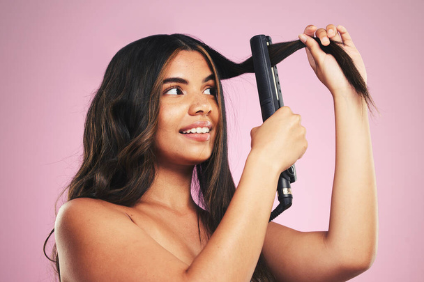 Γυναίκα, μαλλιά και φροντίδα με σίδερο στο στούντιο για την ομορφιά, καλλυντική θεραπεία και λάμψη σε ροζ φόντο. Πρόσωπο νεαρού μοντέλου, χτένισμα και θερμαντικός εξοπλισμός ηλεκτρικών εργαλείων αισθητικής υφής. - Φωτογραφία, εικόνα