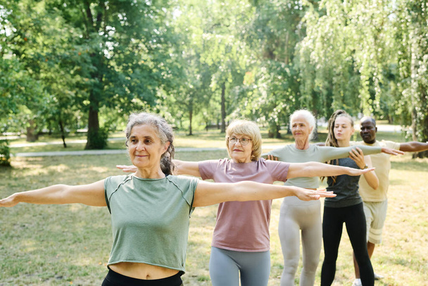 Senioren stehen in Reih und Glied und machen gemeinsam mit Trainer Übungen im Freien - Foto, Bild