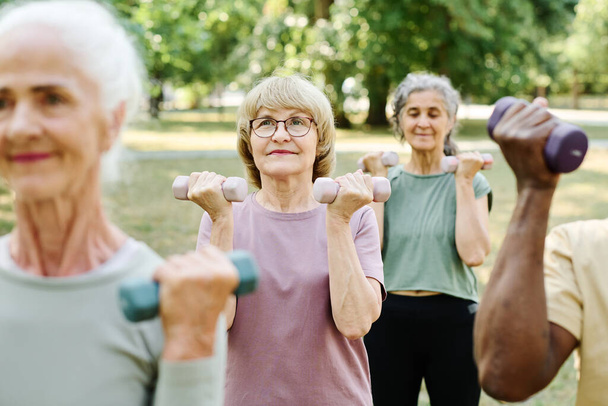 Старшие люди занимаются спортом с гантелями на открытом воздухе в парке - Фото, изображение