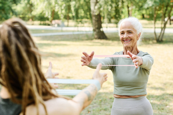 Lächelnde Seniorin trainiert mit Trainer im Freien mit Gummiband - Foto, Bild
