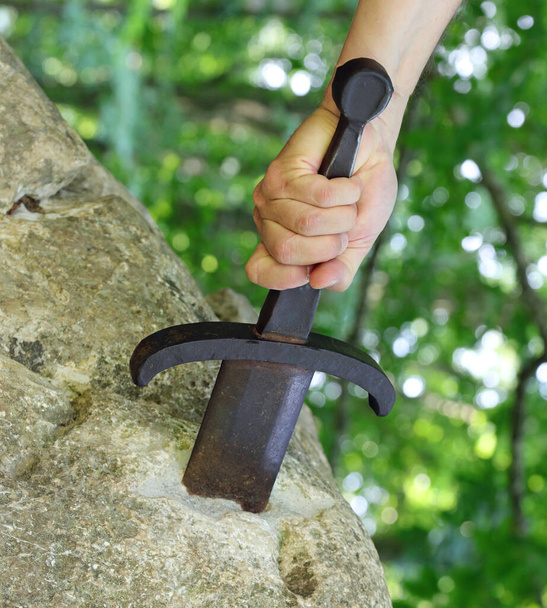 рука насильственно извлекает меч в скале, как в мифологической истории короля Артура - Фото, изображение