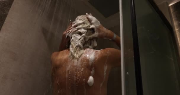 La mujer permanece en la ducha aplicando champú con agua goteando. Tome la ducha y relajarse bajo el agua corriente caliente - Imágenes, Vídeo