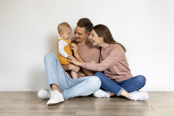Щаслива сім'я трьох з немовлям розважається разом вдома, радісні молоді батьки зв'язуються зі своїми милими чарівним Тоддлером сином або дочкою, сидячи на підлозі, копіювати простір - Фото, зображення